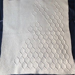 Puede incluir: Una manta de punto beige con un patr&oacute;n geom&eacute;trico de hex&aacute;gonos en un dise&ntilde;o diagonal.