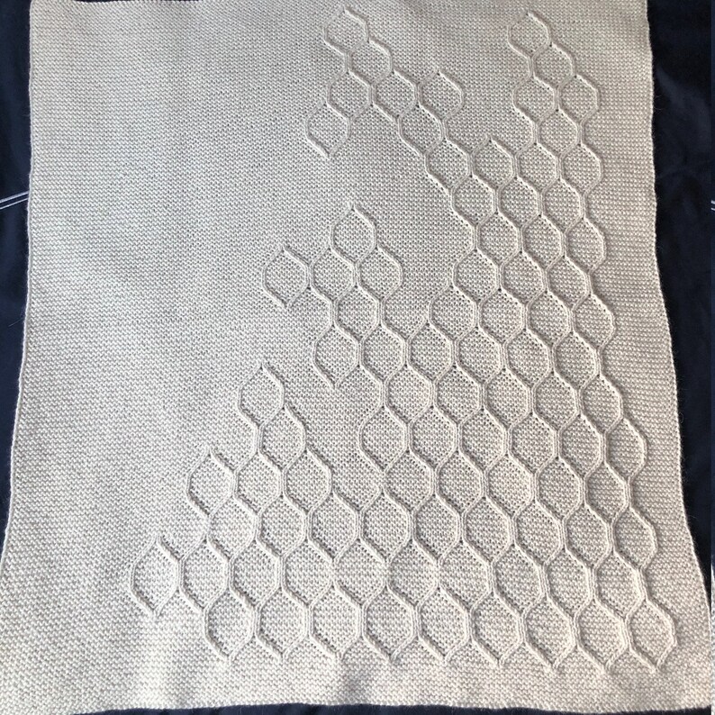 Puede incluir: Una manta de punto beige con un patr&oacute;n geom&eacute;trico de hex&aacute;gonos en un dise&ntilde;o diagonal.