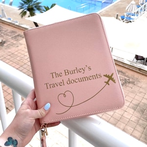 May include: A pale pink travel document holder with a gold zip and wrist strap. The front is inscribed with "The Burley's Travel documents" and a heart and airplane graphic.