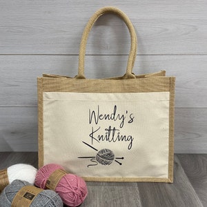 May include: A natural jute tote bag with a white cotton lining. The bag has a black design of knitting needles and yarn with the text "Wendy's Knitting".