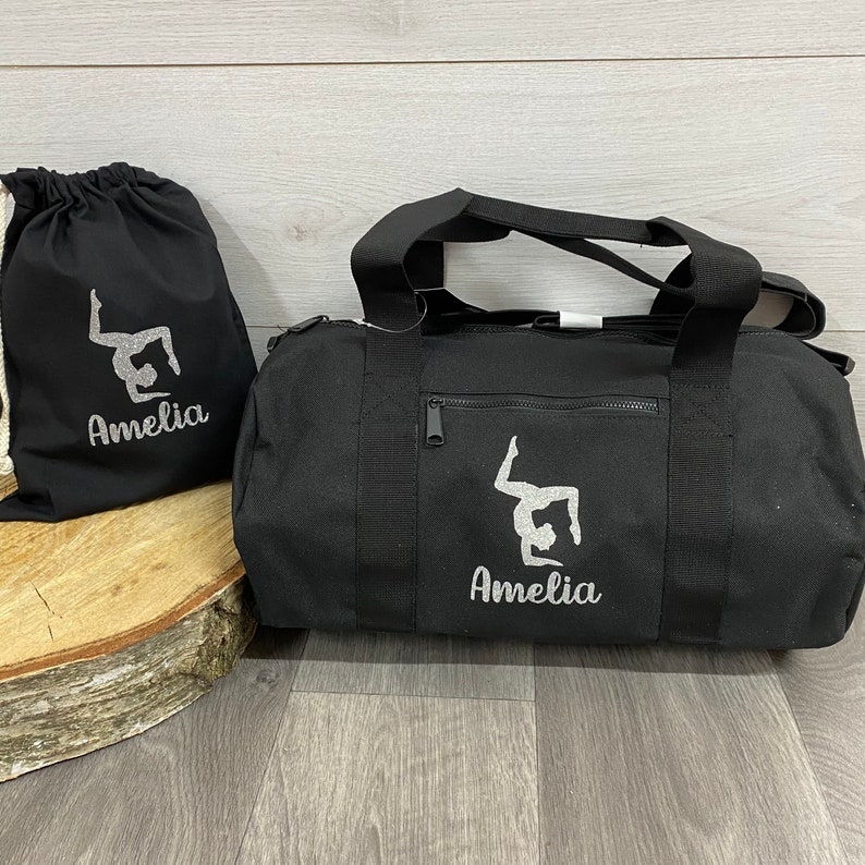 May include: Black gym bag with a zipped pocket and a silver glitter design of a gymnast with a personalised name printed underneath. A smaller black drawstring bag with the same design is also pictured and can be purchased at an additional cost