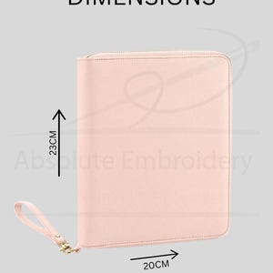 May include: A light pink zippered portfolio case with a matching wrist strap. The case features a textured surface and is labelled with the dimensions 23cm in height and 20cm in width. The text DIMENSIONS and Absolute Embroidery are visible.