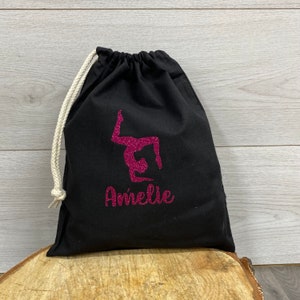 May include: Black drawstring bag with a pink glitter gymnast silhouette and a personalised name underneath the gymnast in pink glitter.