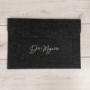 May include: A black felt laptop sleeve with a white embroidered name "Dr. Maguire" on the front.