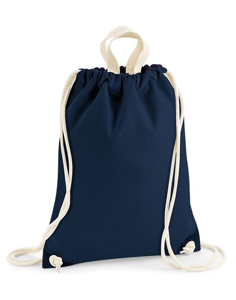 May include: A navy blue drawstring backpack with cream-colored rope straps. The bag is made of a smooth fabric and has a simple, minimalist design. The drawstring closure is visible at the top, and the straps are knotted at the bottom.
