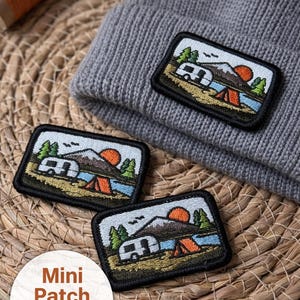 Może przedstawiać: Trzy haftowane mini naszywki z motywem kempingowym. Każda naszywka przedstawia kampera, górę, słońce i namiot. Naszywki mają wymiary około 5 x 3,3 cm. Jedna naszywka jest przymocowana do szarej czapki.