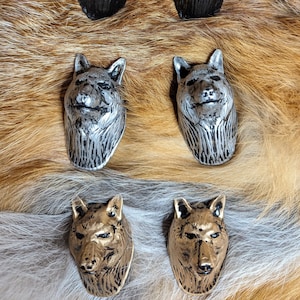 May include: Six wolf head bottle stoppers in three different finishes: black, silver, and gold. The stoppers are displayed on a furry surface.