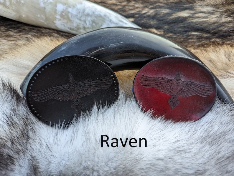 May include: Two leather coasters with a raven design. One coaster is black and the other is red.