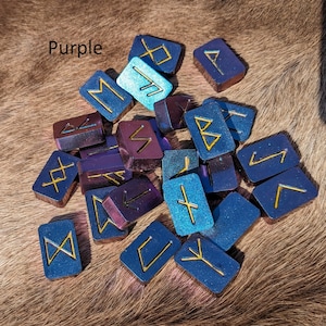 May include: A collection of purple and blue rune stones with gold lettering. The runes are arranged in a random pattern on a brown fur surface. The word "Purple" is written in white text at the top of the image.