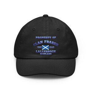 May include: A black baseball cap featuring the text PROPERTY OF CLAN FRASER EST 1743 LALLYBROCH SCOTLAND in blue gradient lettering, centred above a small rectangular blue and white Scottish flag icon on the front panel of the hat.