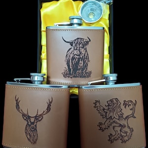 May include: Three brown leather-covered hip flasks with different engraved designs. The flasks are silver with a silver cap. The designs are a Highland cow, a stag, and a lion.
