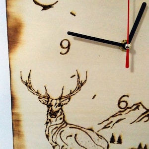 May include: A wooden clock with a deer design, the clock face has Roman numerals and the hands are set to 12:00.