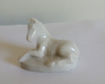 May include: A white porcelain figurine of a zebra lying down. The figurine is detailed with stripes and has a smooth, glossy finish.