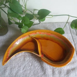 May include: A brown ceramic serving dish with a crescent shape and two divided sections. The dish has a mottled glaze with orange and green accents.