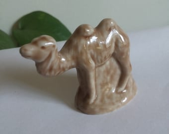 May include: A small, brown ceramic figurine of a camel. The camel is standing on a base and has a hump on its back.