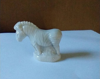 May include: A white ceramic figurine of a zebra standing on a small base. The zebra has black stripes and is in a walking pose.
