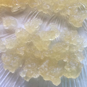 May include: Close-up of a cluster of translucent, yellowish-white, irregularly shaped objects. The objects appear to be clustered together, with a slightly textured surface. The background is a light, translucent material with a subtle pattern.