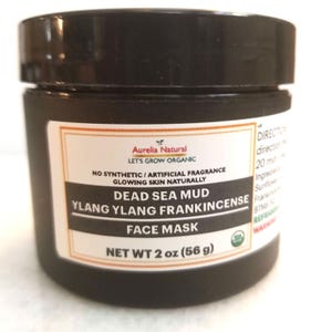 以下が含まれることがあります： Aurelia Naturalのデッドシーマッドフェイシャルマスクの黒い瓶。ラベルには「Ylang Ylang Frankincense」と「Net wt 2 oz（56 g）」の文字が含まれています。瓶には黒い蓋と白とオレンジのラベルが付いています。