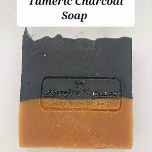May include: A bar of turmeric charcoal soap with a black top layer and a yellow bottom layer. The soap has the words "Aurelia Natural" and "Let's Grow Organic" printed on it.