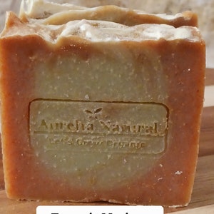 Op de afbeelding: Een oranje en groene zeep met de tekst "Aurelia Natural Let's Grow Organic" aan de voorkant. De zeep is gelabeld "Turmeric Moringa Seamoss Soap".