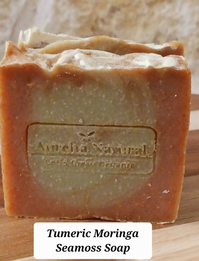Op de afbeelding: Een oranje en groene zeep met de tekst "Aurelia Natural Let's Grow Organic" aan de voorkant. De zeep is gelabeld "Turmeric Moringa Seamoss Soap".
