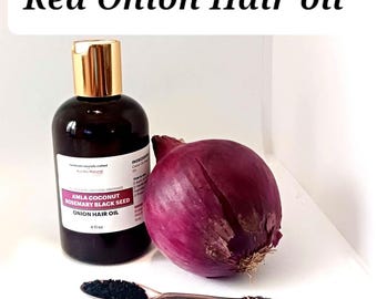 May include: A dark brown bottle of Red Onion Hair Oil with a gold cap, a red onion, and a spoon of black seeds. The bottle label reads "AMLA COCONUT ROSEMARY BLACK SEED ONION HAIR OIL" and "4 fl oz."