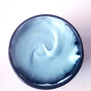 May include: A close-up of a blue face mask in a black container. The mask is thick and creamy.