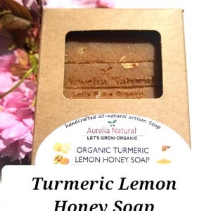 May include: A brown cardboard box containing three bars of organic turmeric lemon honey soap. The soap is labeled "Aurelia Natural" and "Let's Grow Organic". The text "Turmeric Lemon Honey Soap" is displayed below.