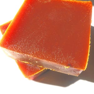Könnte beinhalten: Zwei quadratische Stücke eines rot-orangen Lebensmittels, möglicherweise eine Konfekt oder ein Konservenprodukt, sind gestapelt. Das obere Stück ist scharf, mit einer glatten Oberfläche und einer leicht rauen Kante. Das untere Stück ist teilweise sichtbar.