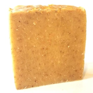 May include: A rectangular bar of handmade soap, light brown in colour with a textured surface. The soap has small, dark specks throughout and a slightly uneven top. The soap is likely scented and suitable for personal hygiene.