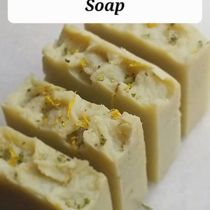Könnte beinhalten: Vier Stück grüne und weiße Seife mit gelben Flocken. Die Seife ist mit "Tamanu Face Body Soap" beschriftet.