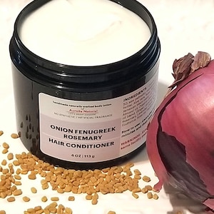 May include: A black jar of "Onion Fenugreek Rosemary Hair Conditioner" with a white cream inside, next to a red onion and scattered seeds. The jar is labeled "4 OZ | 113 g" and "handmade naturally crafted body lotion".