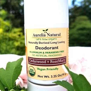 May include: A white deodorant stick with a yellow label. The label reads "Aurelia Natural" and "Cedarwood + RoseMary". It also states "Aluminum & Parabens Free" and "Vegan Friendly". The net weight is 90g.