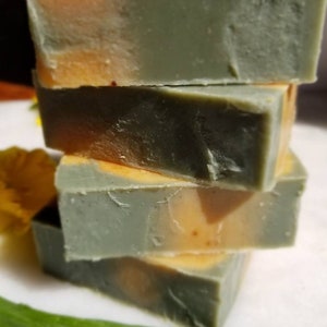 May include: Four bars of handmade soap stacked on top of each other. The soap is a light green and orange color with a swirl pattern.