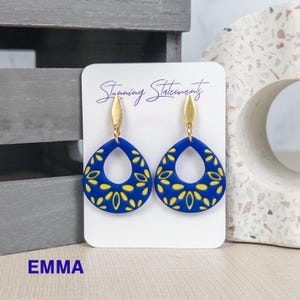 K&ouml;nnte beinhalten: Ein Paar tropfenf&ouml;rmige Ohrringe mit einer leuchtend blauen Basis und einem gelben Blumenmuster. Jeder Ohrring ist an einem goldfarbenen Metallstecker befestigt. Die Ohrringe sind auf einer wei&szlig;en Karte mit der Aufschrift Stunning Statements.