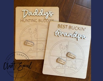 Pode incluir: Dois sinais de madeira com uma silhueta de veado e um design de alvo. O sinal superior diz "Daddy's Hunting Buddies" e o sinal inferior diz "Best Buckin' Grandpa".
