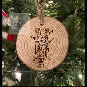May include: A wooden ornament shaped like a tree trunk with a heart carved into it. The heart has the initials "S&C" inside and the year "2015" is carved below the tree.