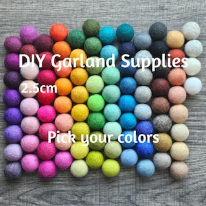 May include: A collection of small, round, felt balls arranged in a grid, featuring a wide spectrum of colors including red, orange, yellow, green, blue, purple, pink, and neutral tones. The text DIY Garland Supplies 2.5cm Pick your colors is visible.