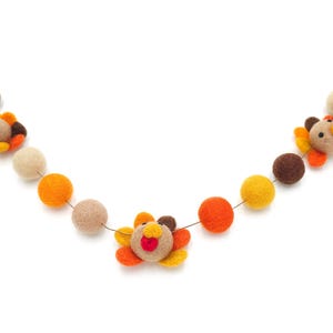 May include: A felt garland with orange, yellow, and brown balls and turkey decorations. The garland is strung on a thin wire.