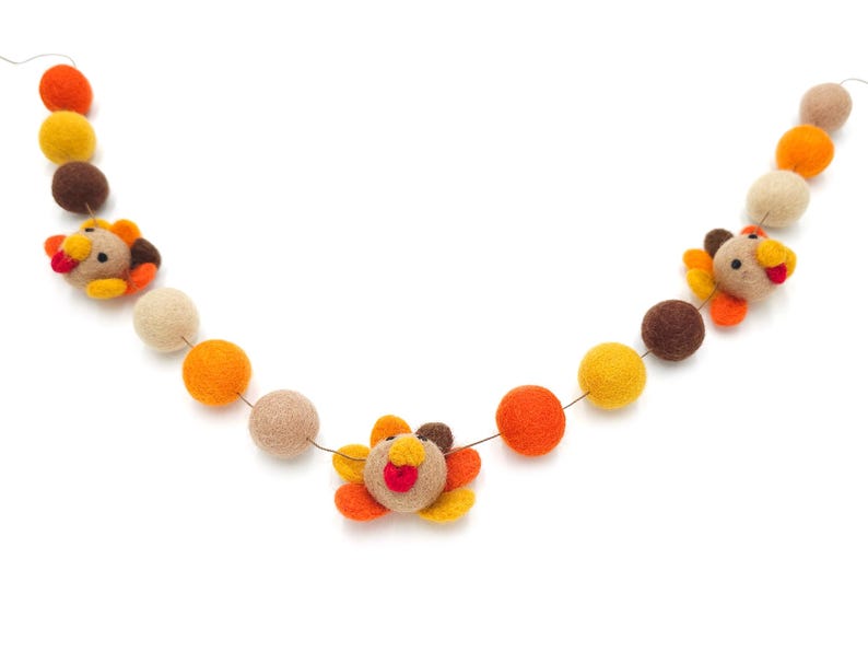 May include: A felt garland with orange, yellow, and brown balls and turkey decorations. The garland is strung on a thin wire.