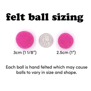 May include: Two pink felt balls, one measuring 3 cm (1 1/8 inches) and the other 2.5 cm (1 inch) in diameter. The balls are shown next to a US quarter for size comparison. "felt ball sizing" is written in black text above the balls. "Each ball is hand felted which may cause balls to vary in size and shape." is written below the balls.