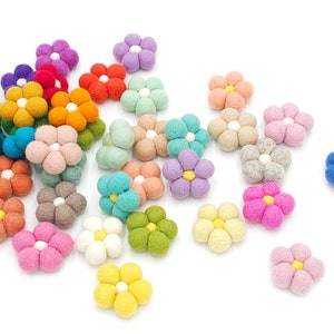 May include: A collection of felt flower embellishments in various colors, including pink, blue, green, yellow, and orange. The flowers have a 5-petal design and a white center.