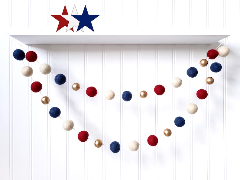 May include: A patriotic garland featuring red, white, and blue felt balls interspersed with gold beads. The garland is suspended against a white backdrop, with star-shaped decorations above. Perfect for festive decor.