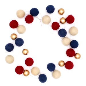 May include: A festive garland featuring alternating red, navy blue, cream-colored felt balls, and gold metallic spheres. The garland is strung on a thin white cord, creating a decorative accent for celebrations and home decor.