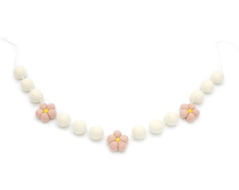 May include: A garland of white felt balls with pink felt flowers, each flower has a yellow center.