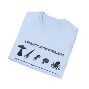 Peut inclure: T-shirt bleu clair avec le texte "A Speculative History of Intelligence" et un graphique noir d'un OVNI, d'un calmar, d'un nautile et d'une pieuvre. Le motif est imprimé sur un t-shirt bleu clair plié.