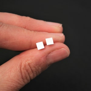 May include: A pair of small, square silver earrings.