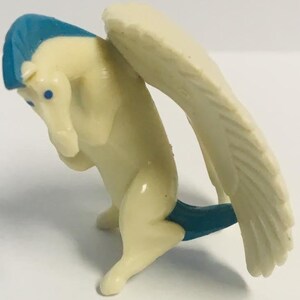 May include: A white plastic figurine of a winged horse with blue wings and a blue mane. The horse is sitting on its hind legs with its front legs raised.