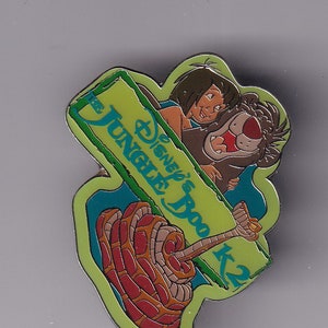 May include: A green and blue enamel pin featuring characters from Disney's Jungle Book. The pin shows Mowgli, Baloo, and Kaa. The text "Disney's Boo Jungle" is on the sign.
