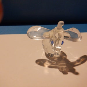 Puede incluir: Una figurita de elefante de cristal transparente con ojos azules. El elefante est&aacute; de pie sobre una superficie blanca.